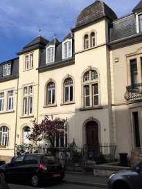 Située sur le prestigieux boulevard de la Pétrusse à Luxembourg-ville, cette magnifique maison de charme datant de 1910, soigneusement préservée dans ses décors d’origine lors des restaurations, présente une surface habitable de ± 252 m² pour une surface totale utile de plus de 300 m², plus terrasse et balcon.
 
La propriété se compose comme suit:
 
Au rez-de-chaussée, le hall d'entrée conservé dans son état d’origine, cartactérisé par des faïences aux murs, carreaux décorés d’époque au sol, cage d'escaliers en bois sculpté et plafond avec moulures authentiques, dessert un spacieux salon-salle à manger en enfilade avec parquet d’époque donnant sur un balcon/terrasse avec vue surprenante sur la vallée de la Pétrusse. La cuisine équipée, adjacente au salon, dispose d’un passe-plat vers la salle à manger. Ce niveau profite d'une belle hauteur sous plafond de 3,40 m.
 
Le 1er étage est introduit par un palier avec vitraux décorés d’origine desservant deux grandes chambres avec moulures authentiques au plafond, un dressing et une salle de bain avec baignoire, douche, lavabo, bidet et wc. Un petit balcon accessible via la plus grande chambre complète l’étage. Parquet d'origine à tout l'étage. Très belle hauteur sous plafond d’environ 3,30 m.
 
Le 2ème étage s’ouvre sur un palier desservant trois chambres et une salle de bain avec poutres apparentes.
 
La maison dispose, au dernier étage, d'un vaste grenier avec Velux sous les combles qui peut être également aménagé.
 
Le 1er sous-sol comprend un salon-séjour, un hall, une chambre, une salle de douche avec lavabo, bidet et wc, une cave à vin, des placards et un local technique - buanderie avec chaudière au gaz et sauna.
 
Le 2ème sous-sol se compose d'un vaste salon-bibliothèque avec poêle à bois, ouvert sur une grande terrasse donnant sur la vallée de la Pétrusse. Un ample jardin arboré complète l’offre.
 
 
Généralités:
 
- Dalles en bois aux 1er et 2ème étages et en béton aux rez-de-chaussée et étages inférieurs; parquet d'origine aux étages supérieurs et au rez-de-chaussée complété par des faïences et carreaux décorés d’époque dans le hall d'entrée, carrelage en faïence dans la cuisine et les pièces des niveaux -1 et -2 ;
- Moulures authentiques aux plafonds des trois étages supérieurs ;
- Chauffage au gaz ;
- Situation idéale, dans l’un des quartiers résidentiels les plus recherchés de Luxembourg-ville : à deux pas des commerces, restaurants, écoles, transports publics (tram, gare, bus) et connexions autoroutières.
 
