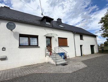 Gepflegtes Einfamilienhaus zum fairen Preis mit großem Grundstück und vielseitigen Nutzungsmöglichkeiten

Dieses gepflegte Einfamilienhaus aus dem Jahr 1949 bietet auf einem großzügigen 750 m² großen Grundstück viel Platz und zahlreiche Möglichkeiten. Die Immobilie verfügt über rund 105 m² Wohnfläche sowie zusätzlich ca. 100 m² Nutzfläche, die sich auf das Nebengebäude und weitere Nebenflächen verteilt.

Ein besonderes Potenzial bietet das Obergeschoss: Hier stehen nochmals rund 30 m² Ausbaufläche zur Verfügung, die sich beispielsweise für zwei zusätzliche Zimmer nutzen lassen. Der vorhandene Speicher ist derzeit nicht ausgebaut.

Wohnbereich und Raumaufteilung

Das Erdgeschoss bietet eine funktionale und angenehm großzügige Aufteilung. Mittelpunkt des Hauses ist das ca. 20 m² große Wohnzimmer. Hinzu kommen eine Wohnküche mit Vorratsraum mit kleiner Einbauküche und ein Badezimmer. Drei Schlafzimmer sind im Obergeschoss.

Die vorhandenen Bodenbeläge bestehen aus Fliesen, Teppich und Holz und verleihen den einzelnen Räumen einen unterschiedlichen Charakter.

Im Untergeschoss befinden sich drei Kellerräume, darunter ein Waschraum. Ebenfalls im Keller ist die Ölzentralheizung mit Brauchwasserversorgung untergebracht. Der Öltank verfügt über ein Fassungsvermögen von 4.000 Litern.

Ausstattung und Modernisierungen

Das Haus wurde laufend gepflegt und teilweise modernisiert:

Baujahr 1949  
ca. 105 m² Wohnfläche  
ca. 100 m² Nutzfläche inklusive Nebengebäude  
ca. 750 m² Grundstück  
ca. 30 m² zusätzliche Ausbaureserve im Obergeschoss  
drei Schlafzimmer  
ca. 20 m² großes Wohnzimmer  
Wohnküche mit kleiner Einbauküche  
Badezimmer  
Vorratsraum  
drei Kellerräume  
Waschraum im Keller  
Ölzentralheizung mit Brauchwasserbereitung  
4.000-Liter-Öltank  
Holzfenster mit Doppelverglasung, überwiegend von 1993, teilweise bis 2009 erneuert  
Natur-Schiefereindeckung des Daches aus dem Jahr 2012  
zwei Garagen  
insgesamt ca. 2 bis 4 Stellplätze im Garagenbereich  
zusätzlich ca. 8 Außenstellplätze  
nicht ausgebauter Speicher  
teilweise Übernahme der vorhandenen Möbel möglich  

Grundstück und Nebengebäude

Das 750 m² große Grundstück bietet insbesondere für Familien, Hobby und zusätzliche Nutzungen viel Platz. Neben dem Wohnhaus gehört ein Nebengebäude mit insgesamt rund 100 m² Nutzfläche zum Anwesen.

Die großzügigen Stell- und Hofflächen sind ein weiterer praktischer Pluspunkt. Neben den zwei Garagen stehen bis zu acht Außenstellplätze zur Verfügung. Damit bietet das Anwesen außergewöhnlich viel Platz für Fahrzeuge, Anhänger, Wohnmobile oder andere Nutzungsmöglichkeiten.

Ausbaupotenzial

Das Haus bietet neben der bestehenden Wohnfläche eine interessante Perspektive für zukünftige Erweiterungen. Im Obergeschoss können auf rund 30 m² zusätzliche Wohn- oder Nutzräume geschaffen werden. Denkbar wäre beispielsweise die Einrichtung von zwei weiteren Zimmern. Die konkrete Umsetzung ist von den baurechtlichen und technischen Voraussetzungen abhängig.

Fazit

Ein gepflegtes Einfamilienhaus in der Eifel mit einem großzügigen Grundstück, umfangreichen Nebenflächen, zwei Garagen und außergewöhnlich vielen Stellmöglichkeiten. Die vorhandene Ausbaureserve bietet zusätzliche Perspektiven und macht die Immobilie sowohl für Familien als auch für Käufer interessant, die viel Platz für Wohnen, Hobby, Fahrzeuge oder Nebennutzung suchen.

Eine solide Immobilie mit großem Grundstück, guter Nutzbarkeit und zusätzlichem Entwicklungspotenzial.