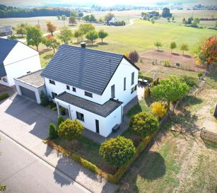 Modernes/ruhig gelegenes Einfamilienhaus in Olsdorf (nahe Luxemburg), mit Doppelgarage, großem Garten und wunderschöner Aussicht/Weitblick

Dieses Einfamilienhaus befindet sich in einer ruhigen Wohnlage von Olsdorf, nur wenige Kilometer von Bitburg und Luxemburg entfernt. Das im Jahr 2016 fertiggestellte Haus bietet auf einer Wohnfläche von 207,79 m² und einem großzügigen Grundstück von 2.113 m² viel Platz für die ganze Familie. Besonders hervorzuheben sind die naturnahe Lage, der große Garten und der freie Blick ins Grüne.

Im Erdgeschoss bildet der offen gestaltete Wohn-, Ess- und Küchenbereich den Mittelpunkt des Hauses. Große Fensterflächen sorgen für helle Räume und bieten direkten Zugang zur Terrasse und zum Garten. Die moderne Miele-Einbauküche mit Kochinsel ist harmonisch in den Wohnbereich integriert. Darüber hinaus befinden sich auf dieser Ebene ein Gäste-WC, ein Gästezimmer mit angrenzendem Bad, ein Hauswirtschaftsraum sowie der Zugang zur Doppelgarage mit Technikraum.

Über eine einläufige Treppe gelangt man ins Obergeschoss. Dort befinden sich eine offene Galerie, ein Schlafzimmer mit Ankleide, zwei weitere Zimmer sowie ein Badezimmer. Zusätzlichen Stauraum bieten die maßgefertigten Einbauschränke auf beiden Etagen. Oberhalb des Obergeschosses befindet sich zudem ein Dachboden, der über eine Einschubtreppe erreichbar ist.

Beheizt wird die Immobilie über eine Erdwärmepumpe in Kombination mit einer Fußbodenheizung. Im gesamten Haus sind hochwertige Fliesenböden sowie Aluminiumfenster mit Raffstores verbaut, ergänzt durch Natursteinfensterbänke im Innen- und Außenbereich. Die Ausstattung befindet sich in einem gepflegten, neuwertigen Zustand und entspricht einem modernen Wohnstandard. Das Haus wird teilweise möbliert übergeben. Im Wohn- und Essbereich ist zudem bereits ein Anschluss für einen Holzofen vorhanden, sodass dieser bei Bedarf nachgerüstet werden kann.

Der Außenbereich bietet eine große Terrasse, einen weitläufigen Garten sowie einen unverbaubaren Blick auf die umliegende Landschaft. Der Großteil des Grundstücks ist dabei umzäunt, was perfekt für Hundebesitzer:innen ist. Zusätzlich stehen neben der Doppelgarage weitere Stellplätze zur Verfügung.

Dank der energieeffizienten Bauweise erreicht das Haus die Energieeffizienzklasse A+ bei einem Endenergiebedarf von 17,6 kWh/(m²·a).

Eine Immobilie für alle, die ruhiges Wohnen in ländlicher Umgebung schätzen und gleichzeitig die Nähe zu Bitburg und Luxemburg nutzen möchten.

Mit dem neuwertigen Zustand der Immobilie haben Sie quasi einen Neubau, sparen aber viel Geld im Vergleich zu einem Neubau in diesem hochwertigen Standard. Das alles in einer wunderschönen Höhenlage zu einem fairen Preis.