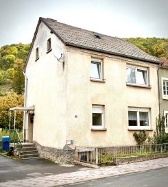 Kleines Einfamilienhaus mit Potenzial in Waxweiler – solide Basis für kreative Ideen!

Dieses Einfamilienhaus aus dem Jahr 1960 bietet eine charmante Grundlage für alle, die ein kompaktes Eigenheim mit Ausbaupotenzial suchen. Auf ca. 63 m² Wohnfläche und einem Grundstück von 73 m² lässt sich mit etwas Liebe zum Detail ein gemütliches Zuhause gestalten.

Objektdetails
Baujahr: 1960
Wohnfläche: ca. 63 m²
Grundstück: ca. 73 m²
Zimmer: 3
Bodenbeläge: Holzdielen und Fliesen
Badezimmer: mit Dusche
Fenster: PVC-Isolierverglasung
Heizung: Elektro-Nachtspeicher
Dach: Kunstschiefereindeckung
Sat-Anlage: vorhanden
Keller: Teilunterkellert
Einbauküche: klein, aber gepflegt

Beschreibung

Das Haus überzeugt durch seine solide Grundstruktur und vielseitige Nutzungsmöglichkeiten. Mit kreativen Ideen kann hier ein behaglicher Wohnraum entstehen – perfekt geeignet für Singles, Paare oder als Zweitwohnsitz. Die vorhandene Einbauküche und die isolierverglasten Fenster bieten bereits eine gute Basis für eine individuelle Gestaltung.

Ein kompaktes Haus mit solider Basis und viel Potenzial für kreative Wohnideen – ideal für alle, die ein kleines, eigenständiges Zuhause in ruhiger Lage suchen.